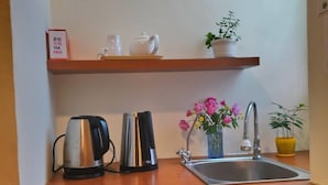 A compact kitchen with a coffee maker, kettle, and a small sink. A refrigerator is below the counter, and a framed picture hangs above the sink. - Flower Bed&Breakfast is now Ikegami (Chishang)