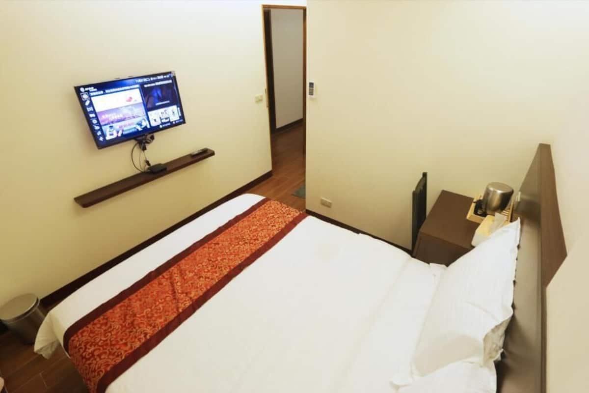 A hotel room with a bed, a TV mounted on the wall, a bedside table, and a nightstand.