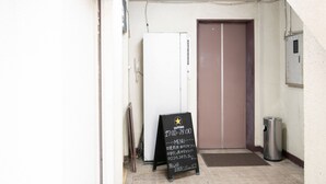 A hallway with a closed door, a trash can, and a black signboard with text.
