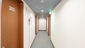 A hallway with a carpeted floor, wooden doors, a phone on the wall, and a ceiling light.