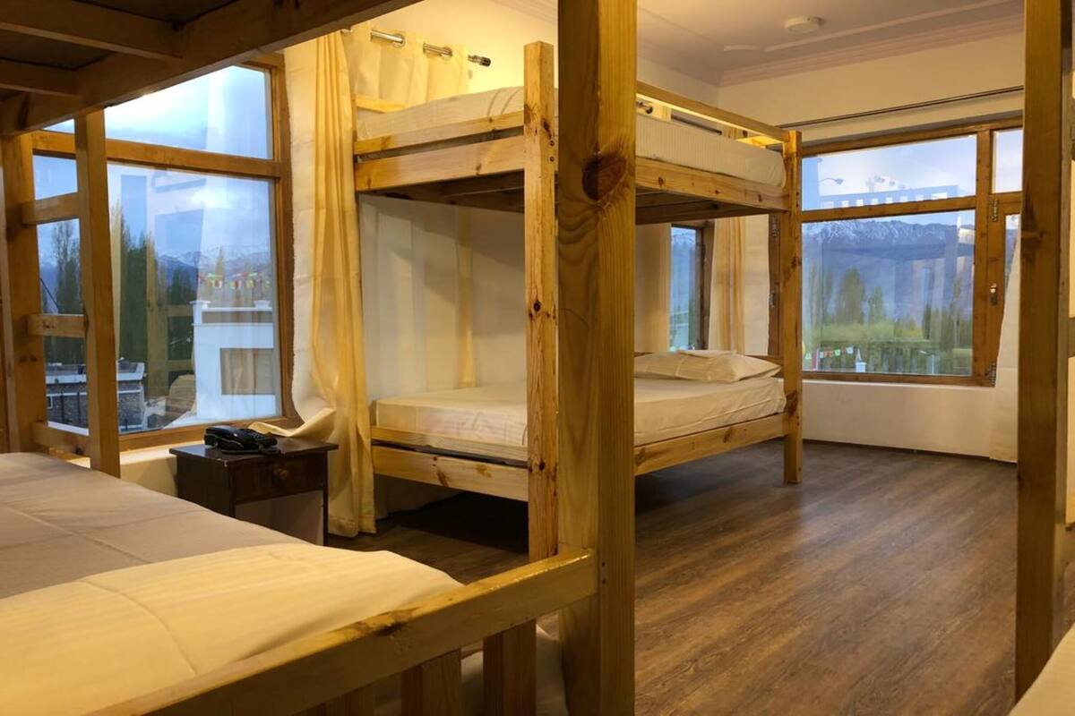 A room with bunk beds, wooden floors, and large windows offering a view of the outdoors.