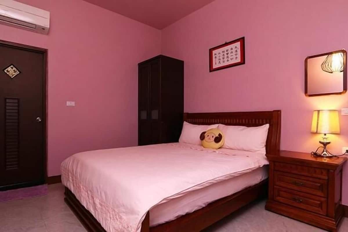 A bedroom with a bed, a nightstand with a lamp, a wardrobe, and a door with a lock.