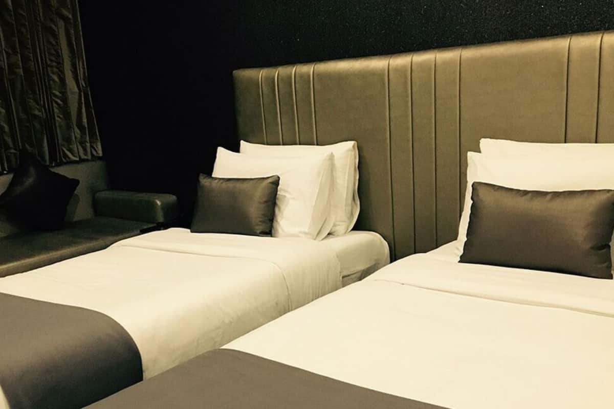 A hotel room with two beds, each with white linens and dark pillows.