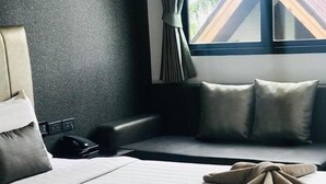 A hotel room with two beds, a sofa, and a window with curtains. - The TJ Resort (Pattaya)