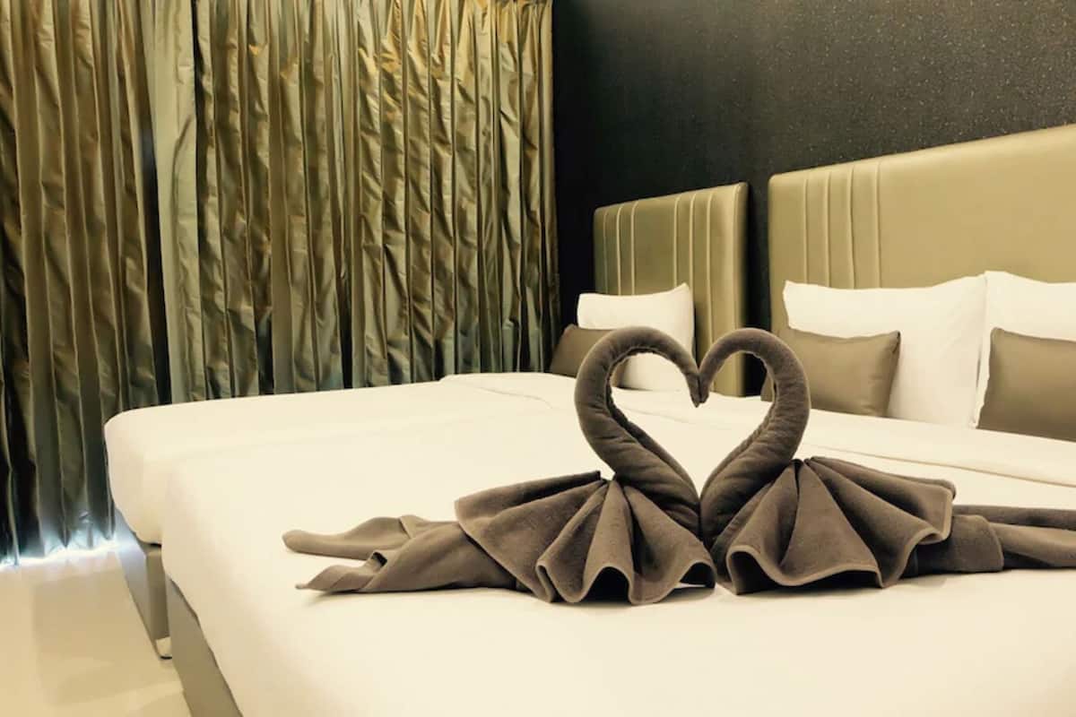 A hotel room with a bed, a heart-shaped towel arrangement, and a curtain.