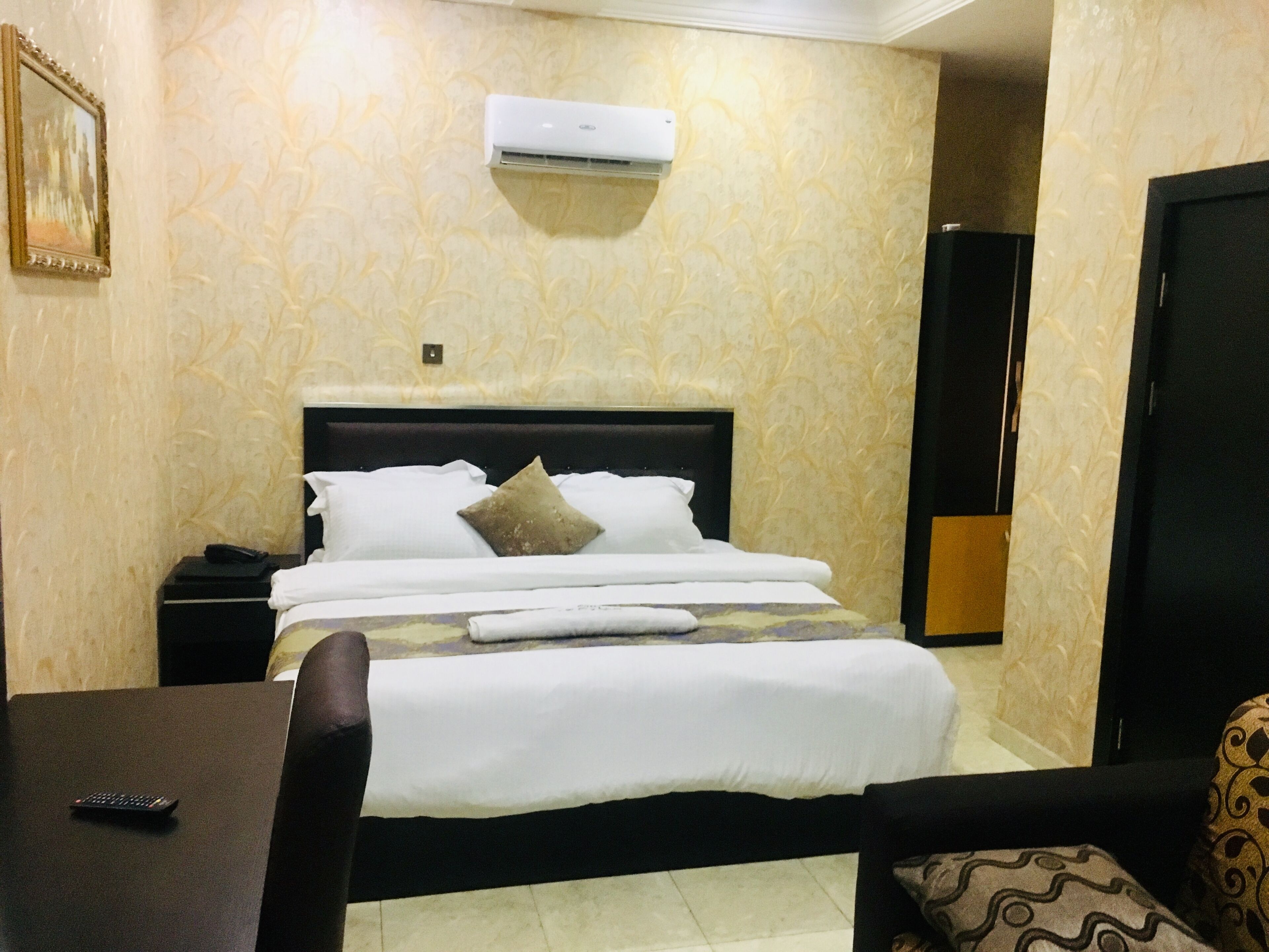 A hotel room with a bed, bedside table, and an air conditioning unit on the wall.