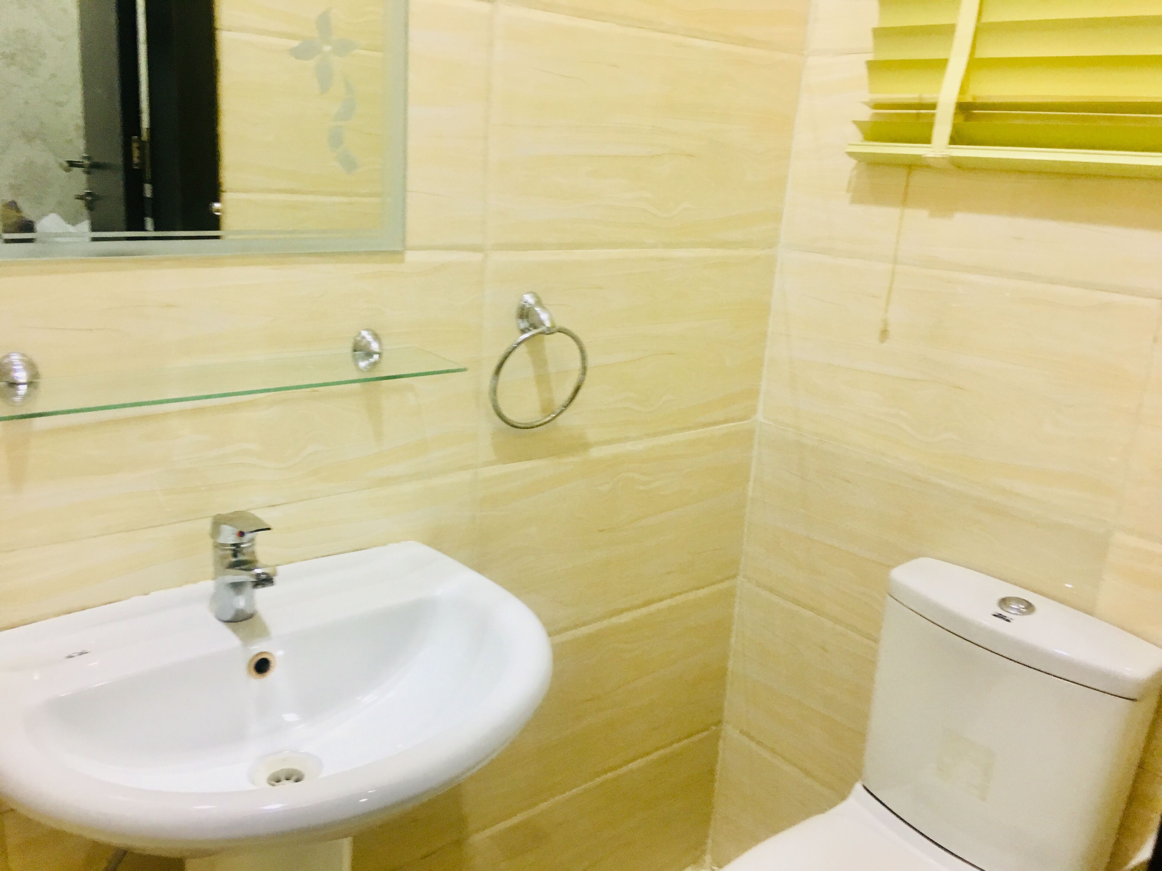 A bathroom with a white sink, a toilet, and a glass shelf above the sink.