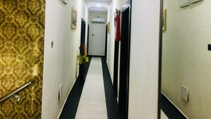 Un pasillo con papel tapiz estampado en una pared, suelo blanco y negro y puertas a ambos lados.