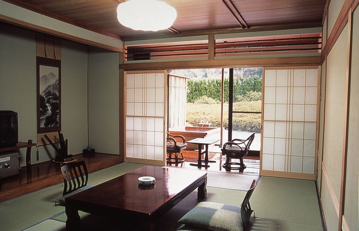 Une pièce de style japonais traditionnel, avec un sol recouvert de tatamis, une table basse, des chaises et des portes coulissantes donnant sur un jardin.
