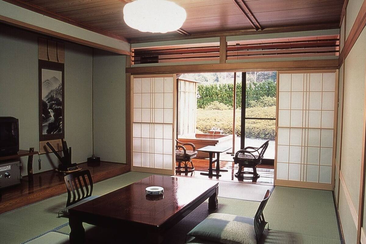 Une pièce de style japonais traditionnel, avec un sol recouvert de tatamis, une table basse, des chaises et des portes coulissantes donnant sur un jardin.