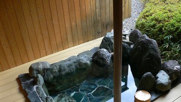 A stone hot tub with a wooden deck and a wooden fence in the background. - Oyado Sansui (Achi)