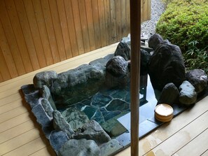 A stone hot tub with a wooden deck and a wooden fence in the background. - Oyado Sansui (Achi)