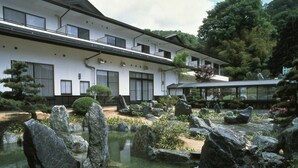 A traditional Japanese-style building with a koi pond, surrounded by rocks and greenery. - Oyado Sansui (Achi)
