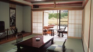 A traditional Japanese-style room with tatami flooring, a low wooden table, and sliding doors leading to an outdoor area. - Oyado Sansui (Achi)