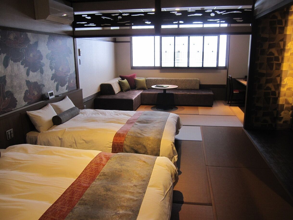 Une chambre d’hôtel avec deux lits, un canapé, une petite table et une vue sur l’extérieur grâce à de grandes fenêtres.