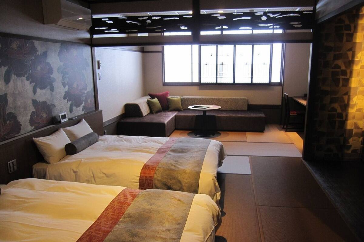 Une chambre d’hôtel avec deux lits, un canapé, une petite table et une vue sur l’extérieur grâce à de grandes fenêtres.