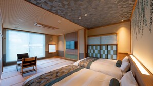 A hotel room with tatami mats, a traditional Japanese-style bed, a television, and a sliding door. - Oyado Sansui (Achi)