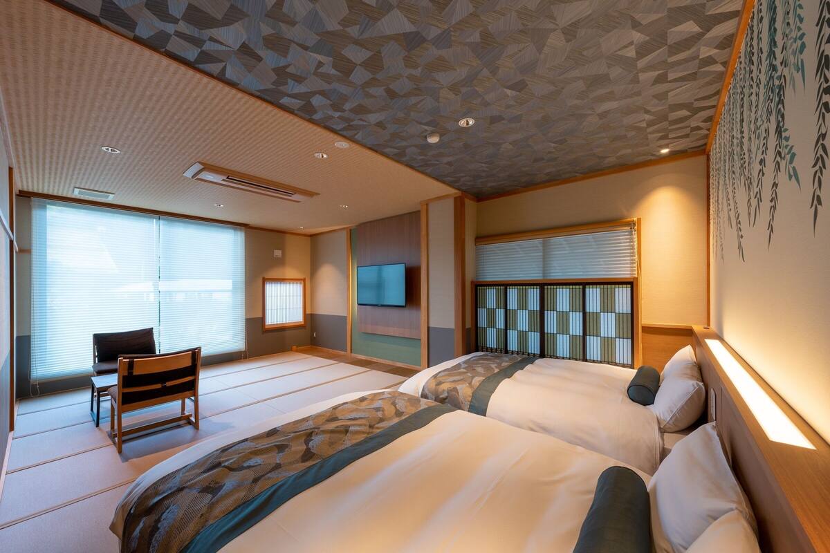 Une chambre d’hôtel avec des tatamis, un lit de style japonais traditionnel, une télévision et une porte coulissante.