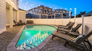 A backyard with a swimming pool, lounge chairs, and string lights. - SEA YOU SOON: Gorgeous Home in Gated Neighborhood w/ Private Pool & Easy Beach Access! (Miramar Beach)