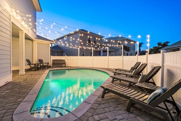 A backyard with a swimming pool, lounge chairs, and string lights. - SEA YOU SOON: Gorgeous Home in Gated Neighborhood w/ Private Pool & Easy Beach Access! (Miramar Beach)