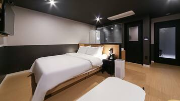 Una habitación de hotel moderna con cama, mesita de noche y un gran ventanal con persianas.