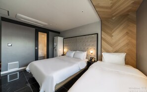 A modern hotel room with two beds, a large padded headboard, and a herringbone wood floor.