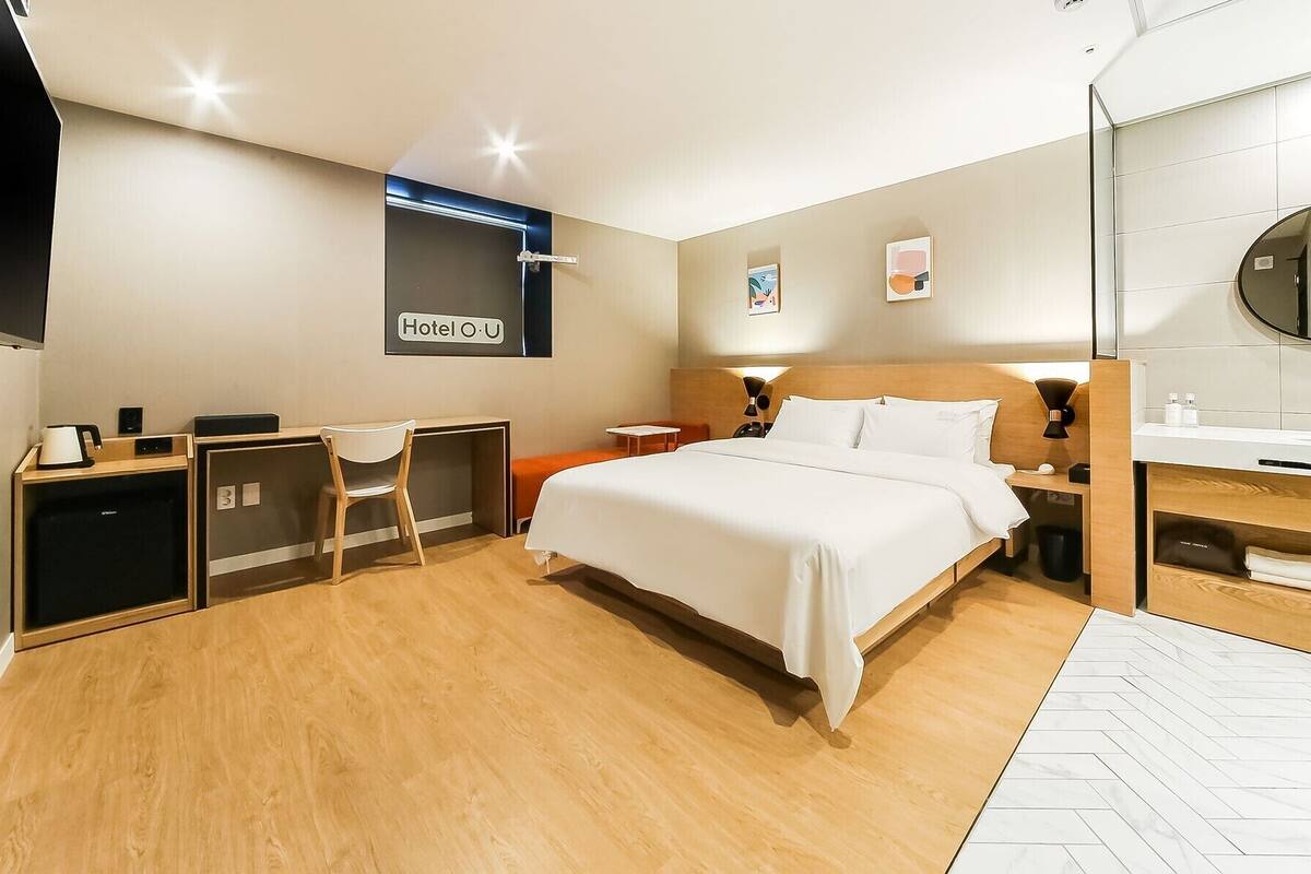 Ein modernes Hotelzimmer mit Bett, Schreibtisch, Stuhl und einem großen Spiegel.