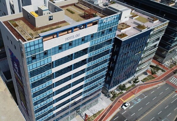 A modern hotel building with a rooftop garden, multiple floors, and a prominent sign for the hotel.