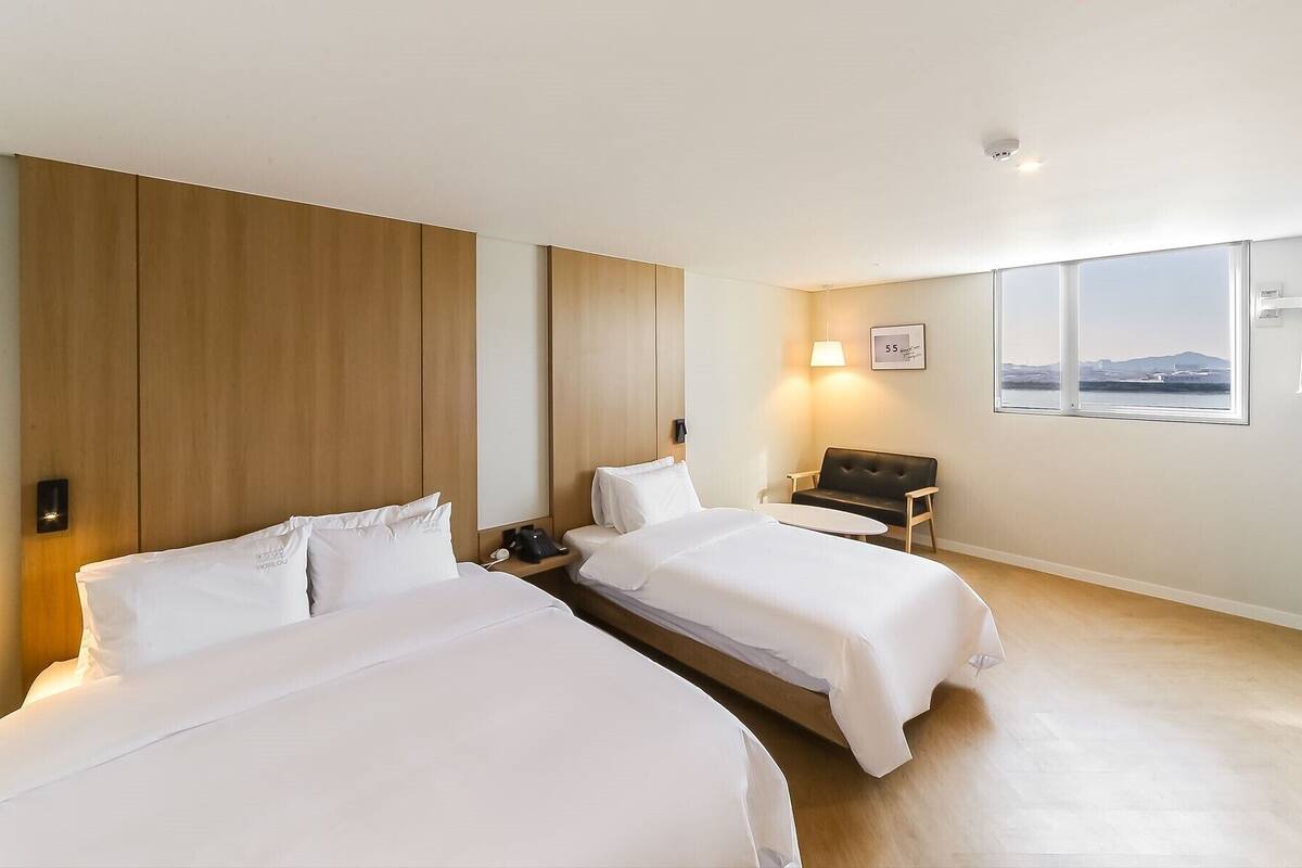 Ein Hotelzimmer mit zwei Betten, einem Schreibtisch, einem Sessel, einem Fenster mit Aussicht und einer Wandlampe.