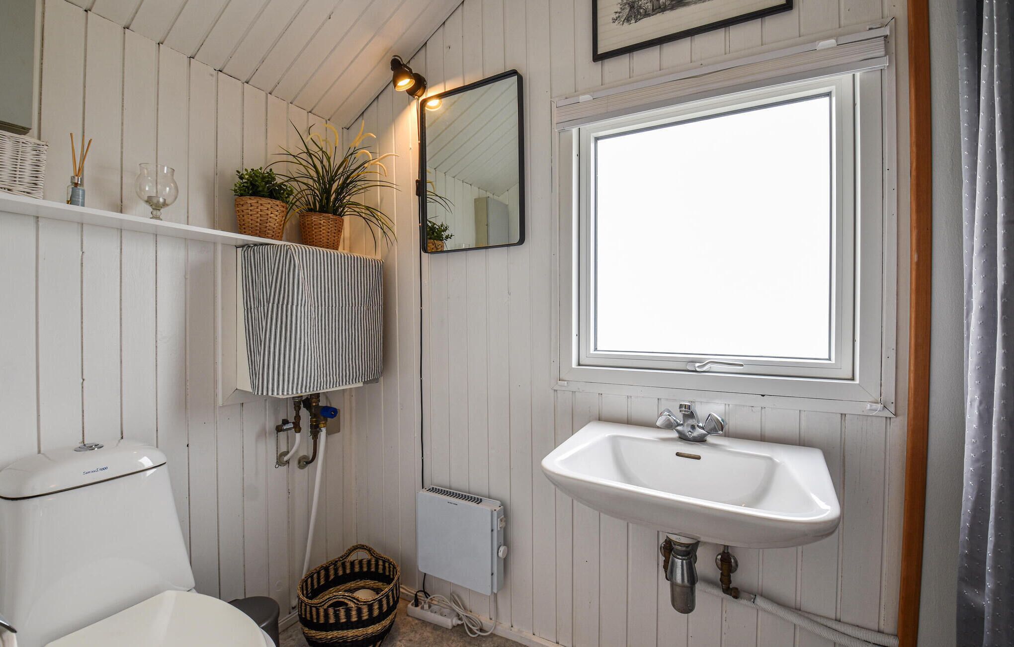 A bathroom with a white sink, a mirror, a toilet, and a window.