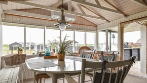 A sunroom with a large table and chairs, a hanging light fixture, and a view of the surrounding area.