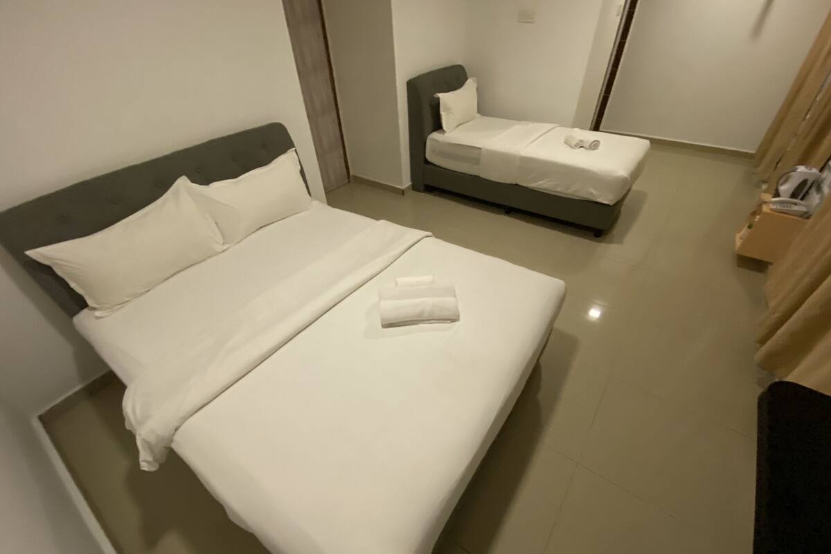 A hotel room with a large bed, a smaller bed, and a wooden nightstand with a lamp.