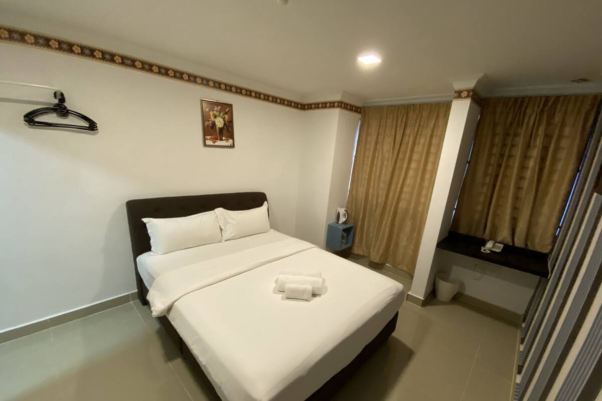 A hotel room with a bed, a nightstand, a mirror, a hanging coat rack, and a painting on the wall.