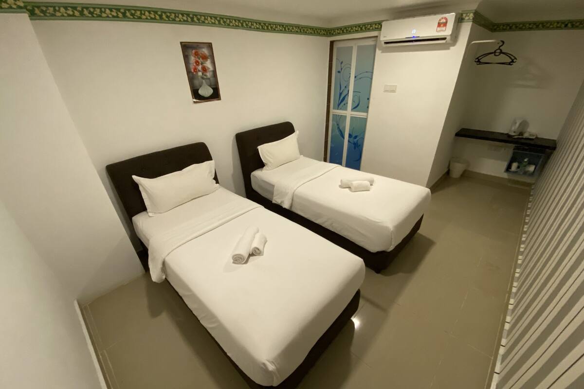 A hotel room with two beds, a painting on the wall, an air conditioning unit, and a small shelf with toiletries.