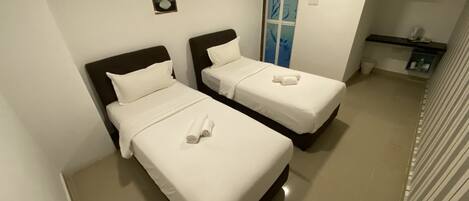 Habitación de hotel con dos camas, un cuadro en la pared, un equipo de aire acondicionado y un pequeño estante con artículos de aseo.