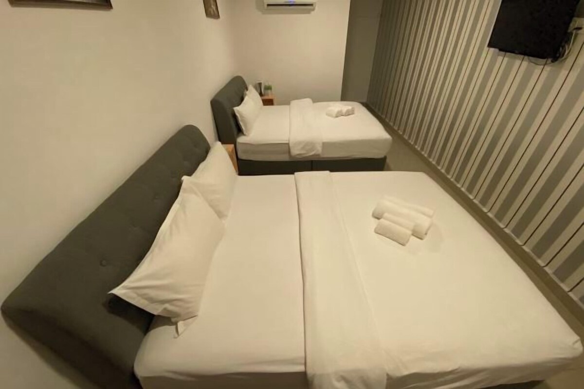 Camera d'albergo con due letti, entrambi con lenzuola e cuscini bianchi, una testata grigia e un comodino con una lampada.
