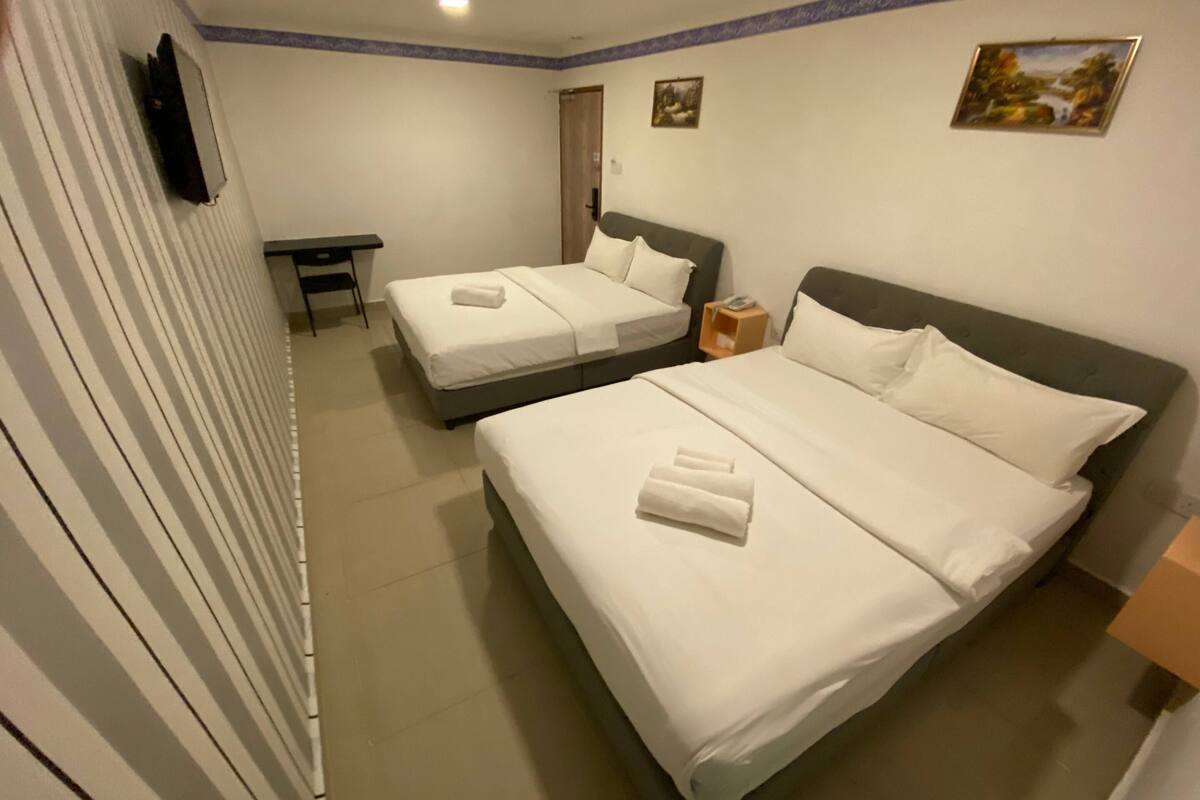 A hotel room with two single beds, a desk, a chair, and a small table.