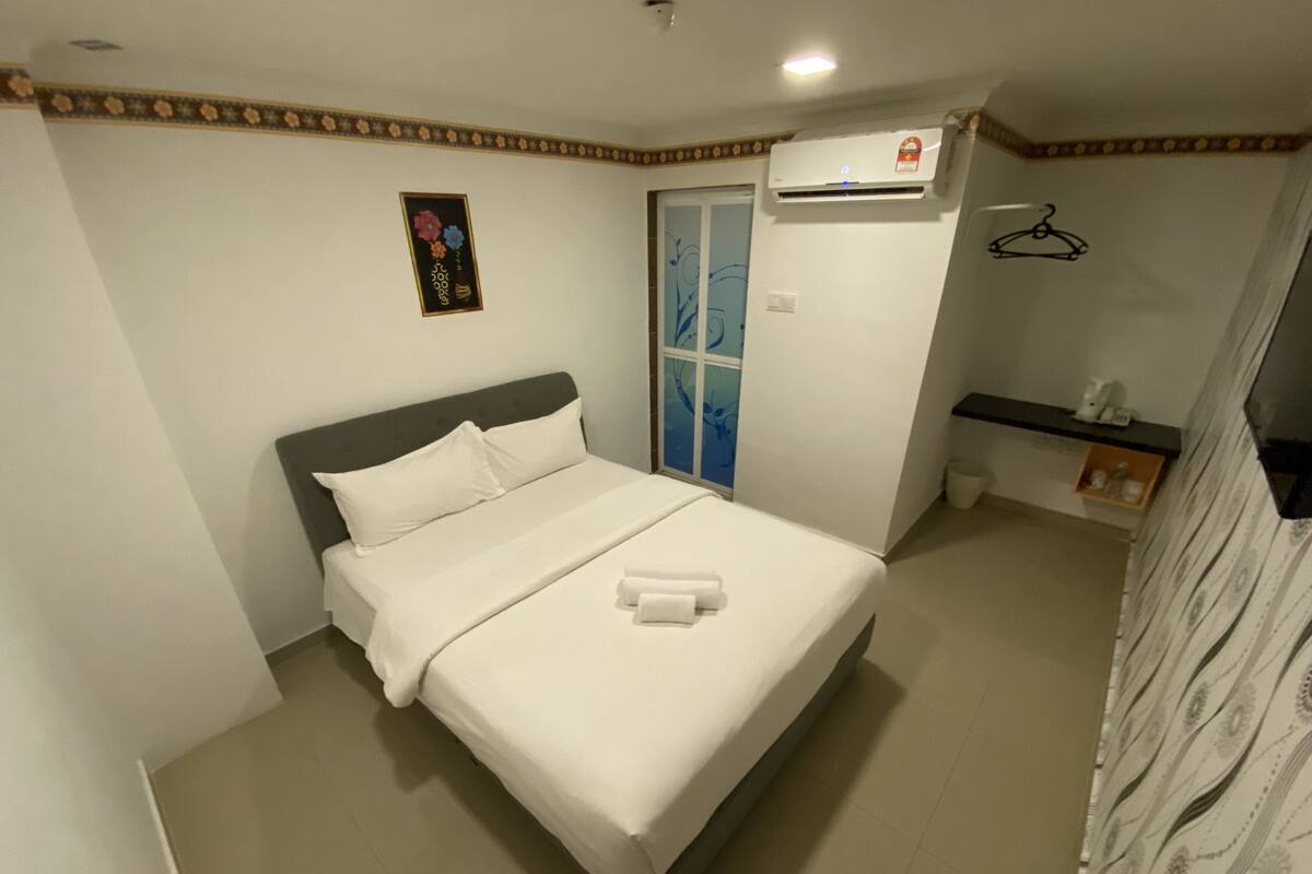 A bedroom with a bed, a wall-mounted air conditioner, a small shelf with toiletries, and a decorative wall piece.