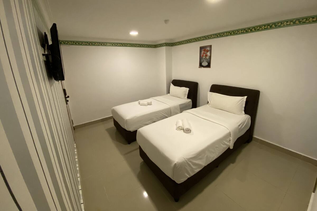 A hotel room with two single beds, a small painting on the wall, and a green decorative border.