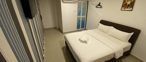 A hotel room with a bed, a TV mounted on the wall, a door, and an air conditioning unit.