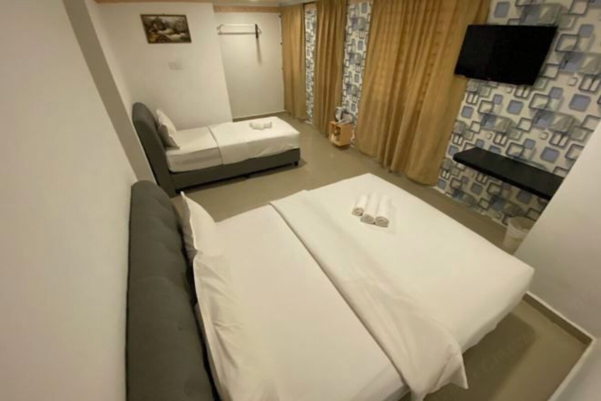 A compact hotel room with a single bed, a sofa, a TV mounted on the wall, and a patterned curtain.