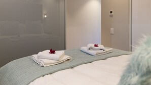 A hotel room with a bed, a blue knitted blanket, and neatly folded towels with a red flower. - The Docklands 509 by CTHA (Cape Town)