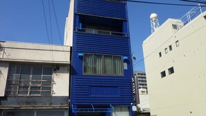 Un edificio de varios pisos con fachada azul, acceso a nivel de calle y una antena parabólica en la azotea.