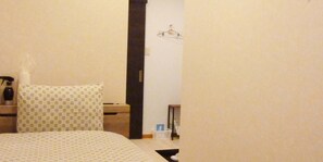 A hotel room with a bed, a nightstand, a dresser, a mirror, and a hanging coat rack.