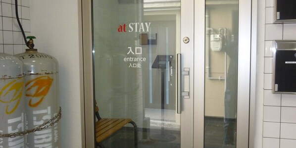 A hotel entrance with a glass door, a bench inside, and two gas cylinders outside.