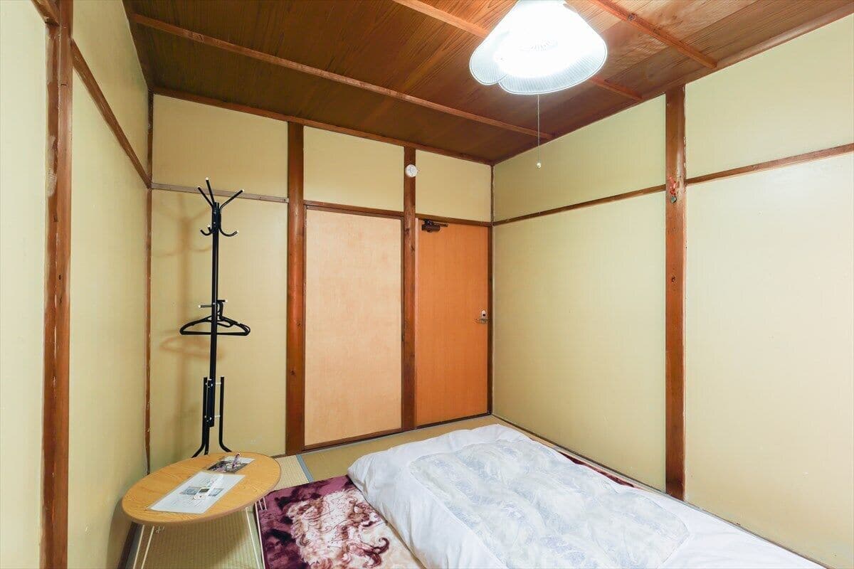 A room with a bed, a coat rack, and a small table with a magazine.