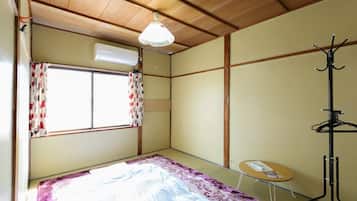Una habitación con una cama, una mesita, un perchero y una ventana con cortinas.