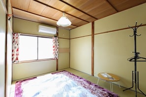 A room with a bed, a small table, a coat rack, and a window with curtains. - Fujinoyado (Kanazawa)
