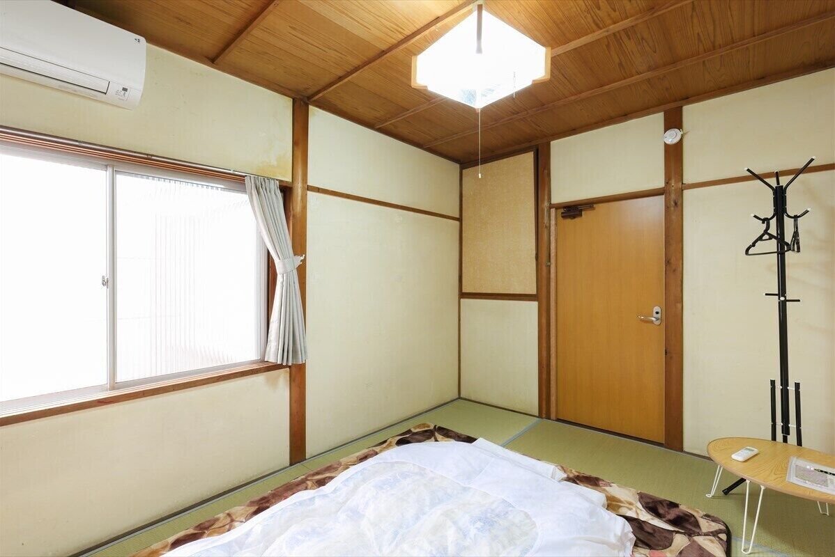 Una habitación tradicional japonesa con suelo de tatami, futón, puerta de madera, panel corredero shoji y ventilador de techo.