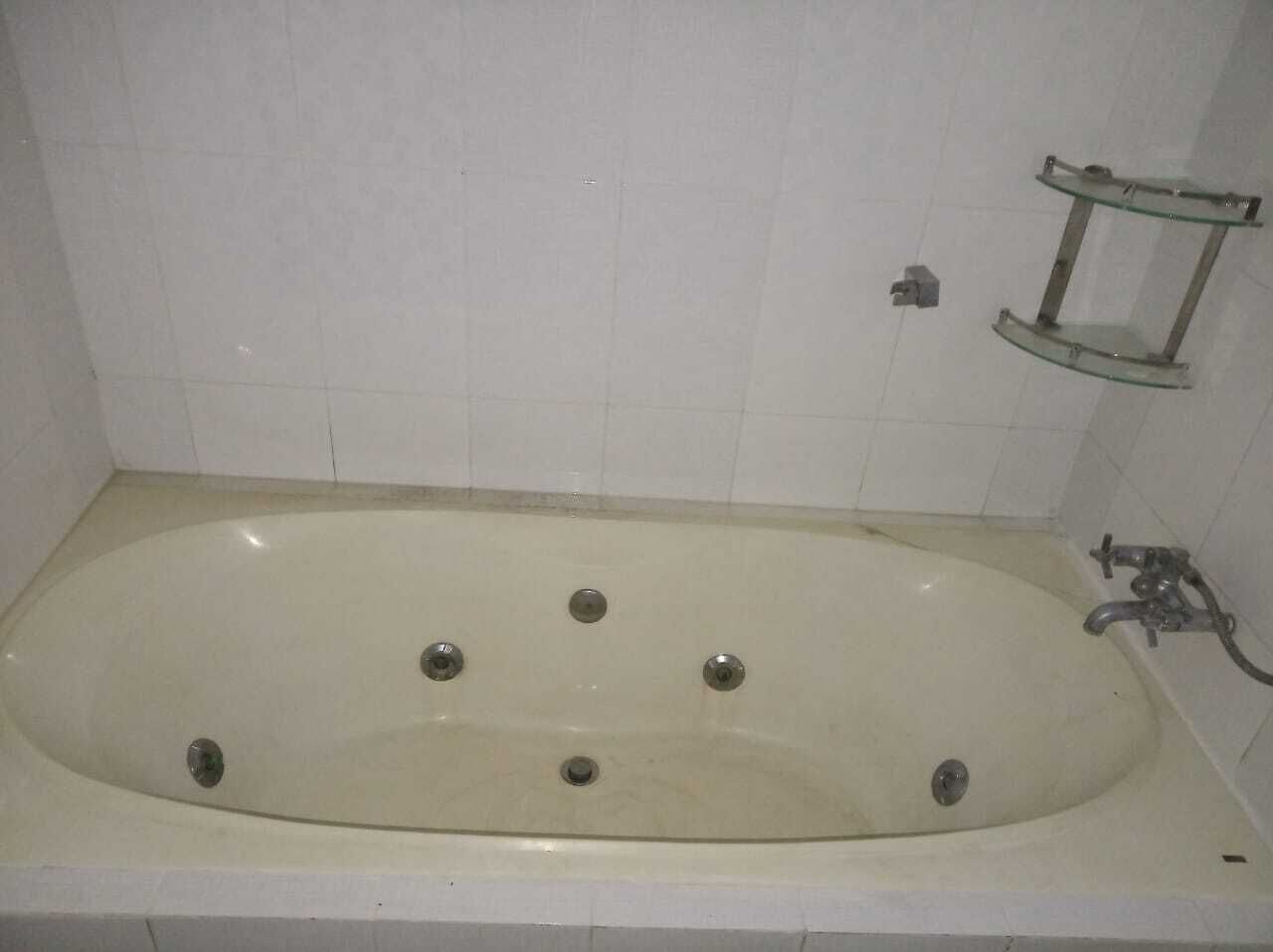 Una bañera estándar con cuatro llaves, un estante de vidrio y un toallero de pared.